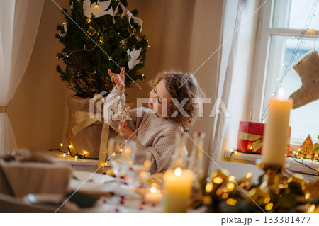 Cheerful small girl indoors at home at Christmas, looking at christmas ornament. Cheerful small girl indoors at home at Christmas, looking at christmas ornament. 133381477