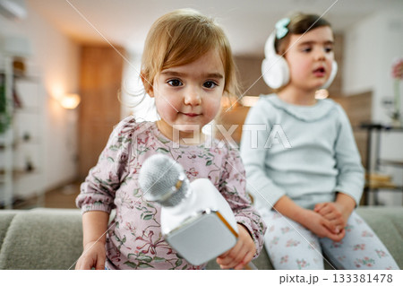 Little girl playing with karaoke microphone at home with her sister 133381478