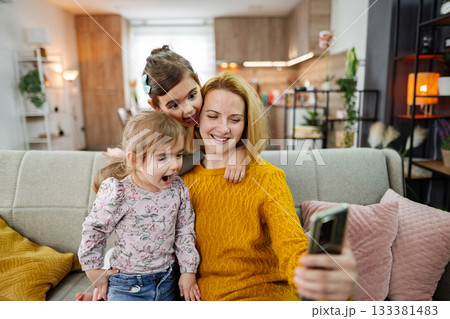 Mother and her three little daughters taking selfies at home Mother and her three little daughters taking selfies at home 133381483