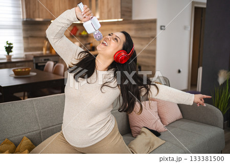 Woman with wireless headphones jumping on sofa and singing at home Woman with wireless headphones jumping on sofa and singing at home 133381500