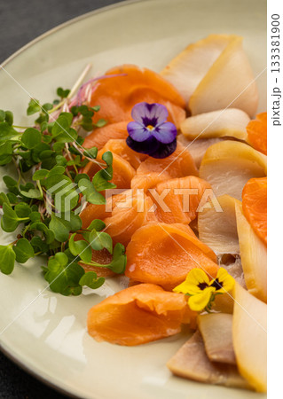 Close up of salmon sashimi with lemon slices and an edible flower on a plate 133381900