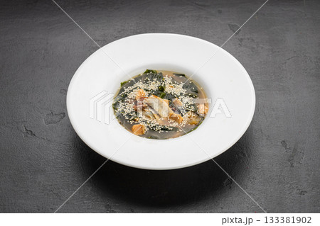 Miso soup with salmon, wakame and sesame in white bowl on dark stone table 133381902