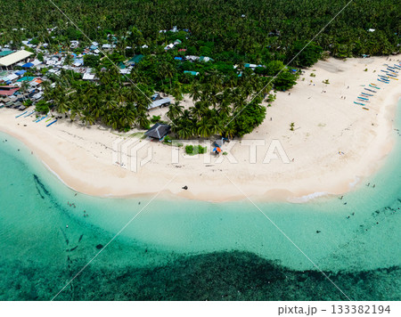 Top view of beach with palm trees and houses along the shoreline beside turquoise water and clear sandy coast. Daku Island. Siargao, Philippines. 133382194