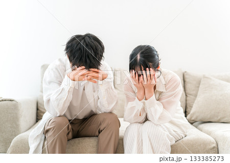 ソファーに座り頭を抱えて落ち込む夫婦,カップル（トラブル,失敗,ショック） 133385273
