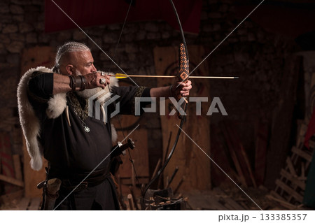 A fierce Viking warrior with long, braided hair and a white beard, dressed in traditional armor with fur, aiming a bow weapon, showcasing strength, heritage, and combat readiness 133385357