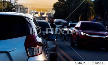 Traffic on the road with many car in the evening time. Bustling movement of many cars in the city. Fuzzy urban environment with street trees and an evening sky. Traffic on the road with many car in the evening time. Bustling movement of many cars in the city. Fuzzy urban environment with street trees and an evening sky. 133385415