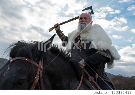 A fierce Viking warrior on horseback, wielding an axe, stands against a dramatic sunset sky with clouds and mountains, embodying strength, exploration, and ancient legend. A fierce Viking warrior on horseback, wielding an axe, stands against a dramatic sunset sky with clouds and mountains, embodying strength, exploration, and ancient legend. 133385418