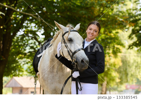 Young woman with her white horse outdoors, equestrian lifestyle, smiling girl and her beautiful horse in nature, friendship and love, happy moments. Young woman with her white horse outdoors, equestrian lifestyle, smiling girl and her beautiful horse in nature, friendship and love, happy moments. 133385545