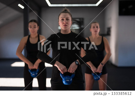 Women performing kettlebell exercises in a modern gym setting during a fitness class in the morning 133385612