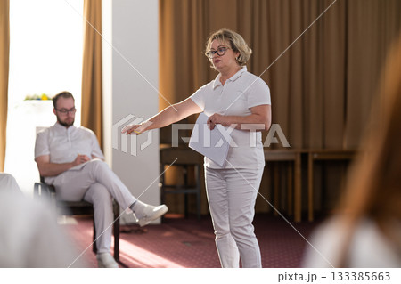 Instructor holding notes and pen while teaching massage therapy class to students, professional training and education in wellness and rehabilitation. Instructor holding notes and pen while teaching massage therapy class to students, professional training and education in wellness and rehabilitation. 133385663