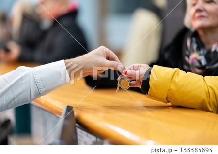 Detail of two people exchanging keys at a reception desk, symbolizing check in, service, hospitality, and property handover Detail of two people exchanging keys at a reception desk, symbolizing check in, service, hospitality, and property handover 133385695