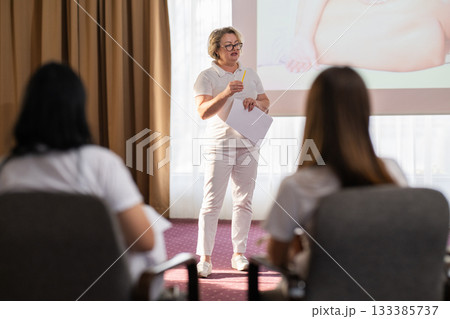 Instructor holding notes and pen while teaching massage therapy class to students, professional training and education in wellness and rehabilitation. Instructor holding notes and pen while teaching massage therapy class to students, professional training and education in wellness and rehabilitation. 133385737