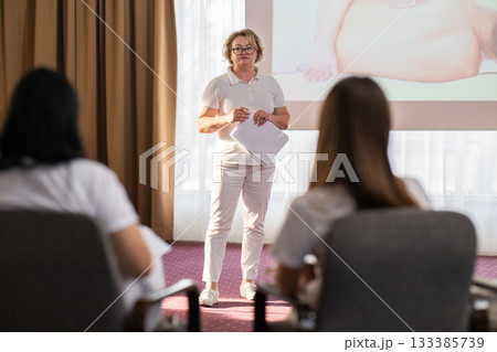 Instructor holding notes and pen while teaching massage therapy class to students, professional training and education in wellness and rehabilitation. Instructor holding notes and pen while teaching massage therapy class to students, professional training and education in wellness and rehabilitation. 133385739