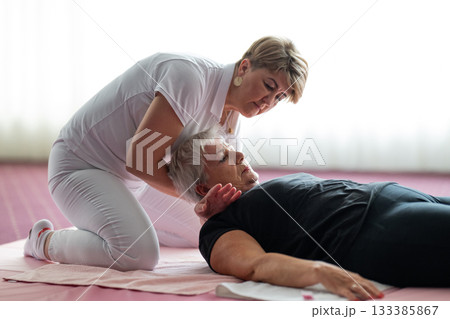 Close up of a physiotherapist holding the head and neck of an older woman lying on a mat during a rehabilitation session. Physiotherapy treatment concept focusing on pain relief, mobility improvement Close up of a physiotherapist holding the head and neck of an older woman lying on a mat during a rehabilitation session. Physiotherapy treatment concept focusing on pain relief, mobility improvement 133385867