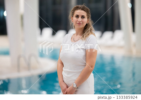 Portrait of a young female wellness coach smiling confidently at an indoor swimming pool, symbolizing health, fitness, and professional guidance. Portrait of a young female wellness coach smiling confidently at an indoor swimming pool, symbolizing health, fitness, and professional guidance. 133385924