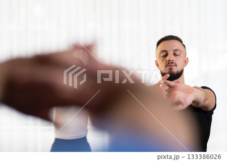 Man stretching his arms forward during a fitness or rehabilitation class indoors. Concept of focus, mindfulness, health, and active lifestyle. 133386026