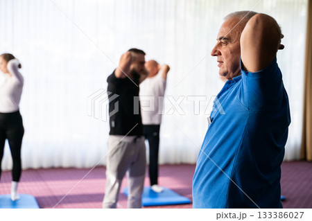 Instructor leading a diverse group of people during a fitness training session with stretching exercises on mats in a bright wellness center Instructor leading a diverse group of people during a fitness training session with stretching exercises on mats in a bright wellness center 133386027