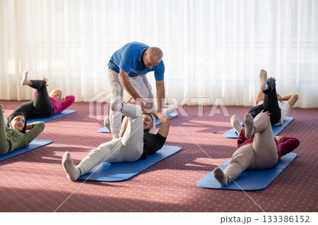 Instructor leading a diverse group of people during a fitness training session with stretching exercises on mats in a bright wellness center 133386152