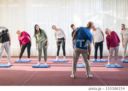 Instructor leading a diverse group of people during a fitness training session with stretching exercises on mats in a bright wellness center 133386154