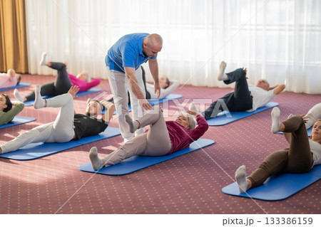 Instructor leading a diverse group of people during a fitness training session with stretching exercises on mats in a bright wellness center 133386159