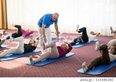 Instructor leading a diverse group of people during a fitness training session with stretching exercises on mats in a bright wellness center Instructor leading a diverse group of people during a fitness training session with stretching exercises on mats in a bright wellness center 133386160