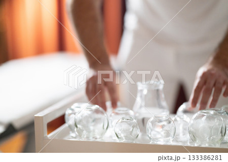 Therapist Preparing Glass Cups for Traditional Cupping Therapy. Close up of therapists hands arranging clean glass cups on a tray before starting a traditional cupping therapy session. Therapist Preparing Glass Cups for Traditional Cupping Therapy. Close up of therapists hands arranging clean glass cups on a tray before starting a traditional cupping therapy session. 133386281