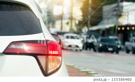 Rear side of white car with turn on brake light. Cars on the opposite side are lined up waiting for the traffic light at the intersection. Blurred of town at day. Rear side of white car with turn on brake light. Cars on the opposite side are lined up waiting for the traffic light at the intersection. Blurred of town at day. 133386460