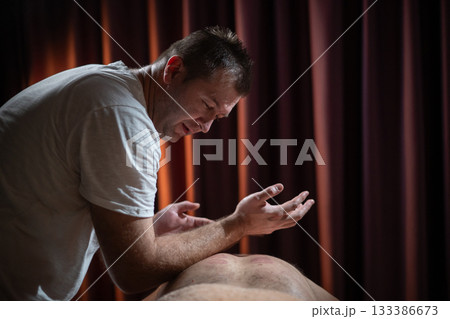Professional male massage therapist performing deep tissue back massage on an older man lying on a massage table covered with a towel. Relaxing wellness treatment in a modern spa room with warm light Professional male massage therapist performing deep tissue back massage on an older man lying on a massage table covered with a towel. Relaxing wellness treatment in a modern spa room with warm light 133386673