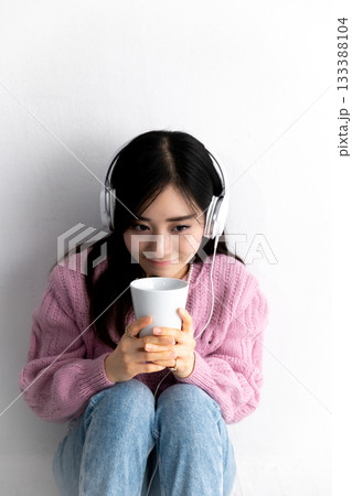 白い壁を背に、ヘッドホンで音楽を聴きながら座って考え事をする若い女性 133388104