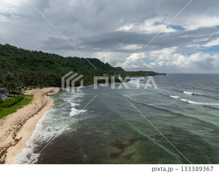 Gentle waves wash onto a sandy shore bordered by tropical trees and hills. Siargao, Philippines. 133389367