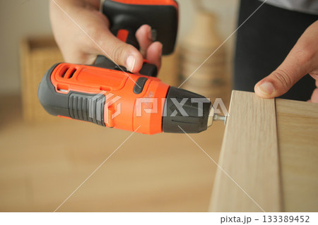Handheld drill being used for furniture assembly indoors 133389452