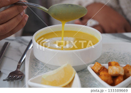 Warm yellow soup served with lemon and croutons 133389669