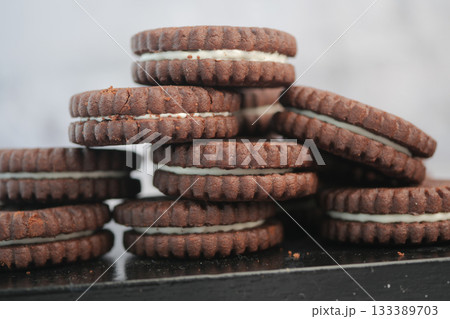 Delicious chocolate sandwich cookies stacked high on a table Delicious chocolate sandwich cookies stacked high on a table 133389703