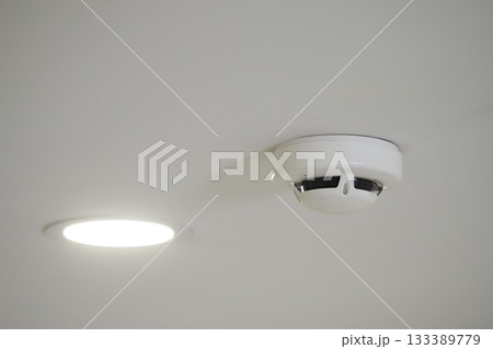 Smoke detector installed on ceiling with ceiling light 133389779
