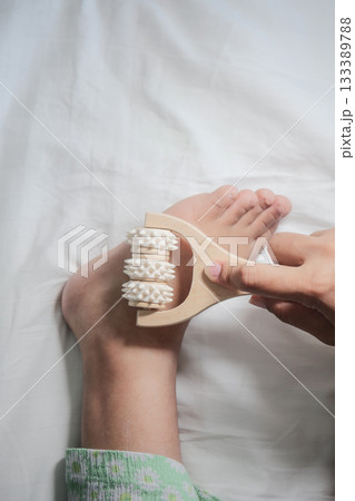 A person uses a wooden foot roller for a soothing massage on child feet. A person uses a wooden foot roller for a soothing massage on child feet. 133389788