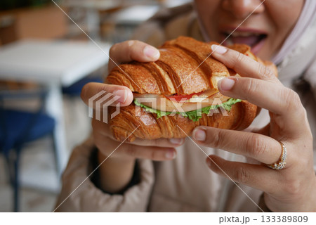 Enjoying a fresh croissant sandwich in a cozy cafe setting 133389809