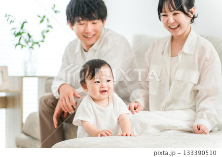 ソファーを使ってつかまり立ちをする赤ん坊と笑顔の家族 133390510