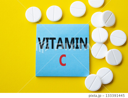 Vitamin C symbol. Concept word Vitamin C on blue note. Beautiful yellow background with pills. Medicine and Vitamin C concept. Copy space Vitamin C symbol. Concept word Vitamin C on blue note. Beautiful yellow background with pills. Medicine and Vitamin C concept. Copy space 133391445