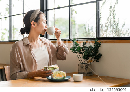 カフェのランチ・ブランチ・朝食でコーヒーを飲みながらサンドイッチを食べるアジア人女性 カフェのランチ・ブランチ・朝食でコーヒーを飲みながらサンドイッチを食べるアジア人女性 133393001