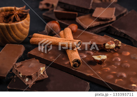 Assorted chocolate bars with nuts, cinnamon sticks and cocoa creating a rich gourmet dessert composition Assorted chocolate bars with nuts, cinnamon sticks and cocoa creating a rich gourmet dessert composition 133393711