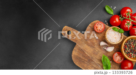 Rustic wooden cutting board with fresh tomatoes, basil, garlic and spices arranged on dark stone background, top view with wide copy space for recipe text, menu design or cooking concepts Rustic wooden cutting board with fresh tomatoes, basil, garlic and spices arranged on dark stone background, top view with wide copy space for recipe text, menu design or cooking concepts 133393726