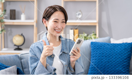 リビングでスマホを操作する女性　サムズアップ 133396108