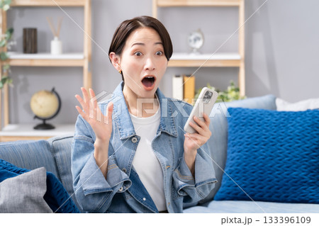 リビングでスマホを持つ女性　驚く 133396109
