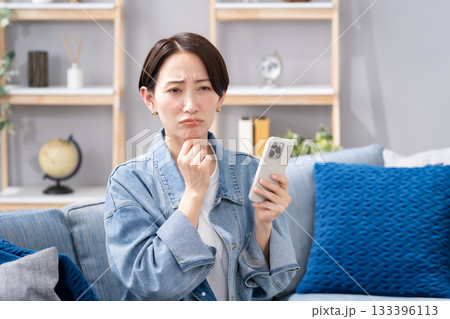リビングでスマホを持つ女性 悩む リビングでスマホを持つ女性 悩む 133396113