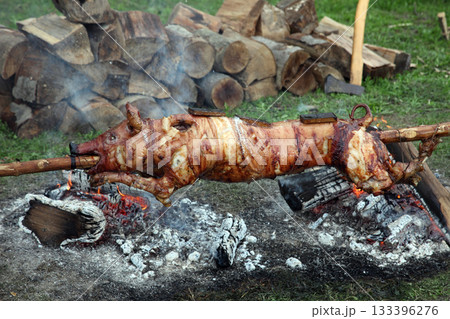 Suckling pig on a rotating spit with fire in the background 133396276