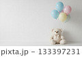 白い壁の前に座るテディベアとパステルカラーの風船 133397231
