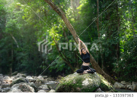 A woman meditating with a waterfall surrounded by nature looking relaxed and stress relieving 133397363