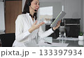 Businesswoman in a white shirt and headset leading a video call from a modern office, presenting with a tablet and gesturing as she discusses strategy and trains remote colleagues 133397934
