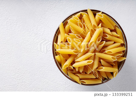 Uncooked Penne Pasta in Ceramic Bowl on White Textured Background Uncooked Penne Pasta in Ceramic Bowl on White Textured Background 133399251