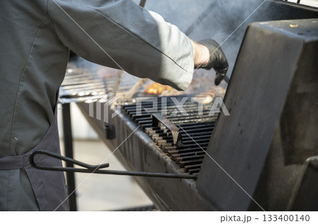 Male chef preparing meat on grill at barbecue party in summer garden 133400140